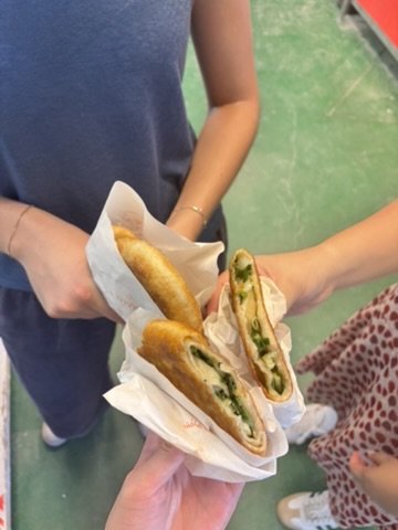 Two people holding sandwiches with fried chicken, lettuce, and other ingredients wrapped in paper.