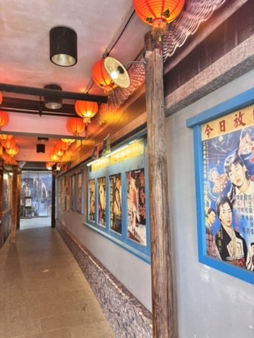 Indoor corridor decorated with red lanterns and vintage posters on the wall, with a mix of traditional and modern Asian decor elements.