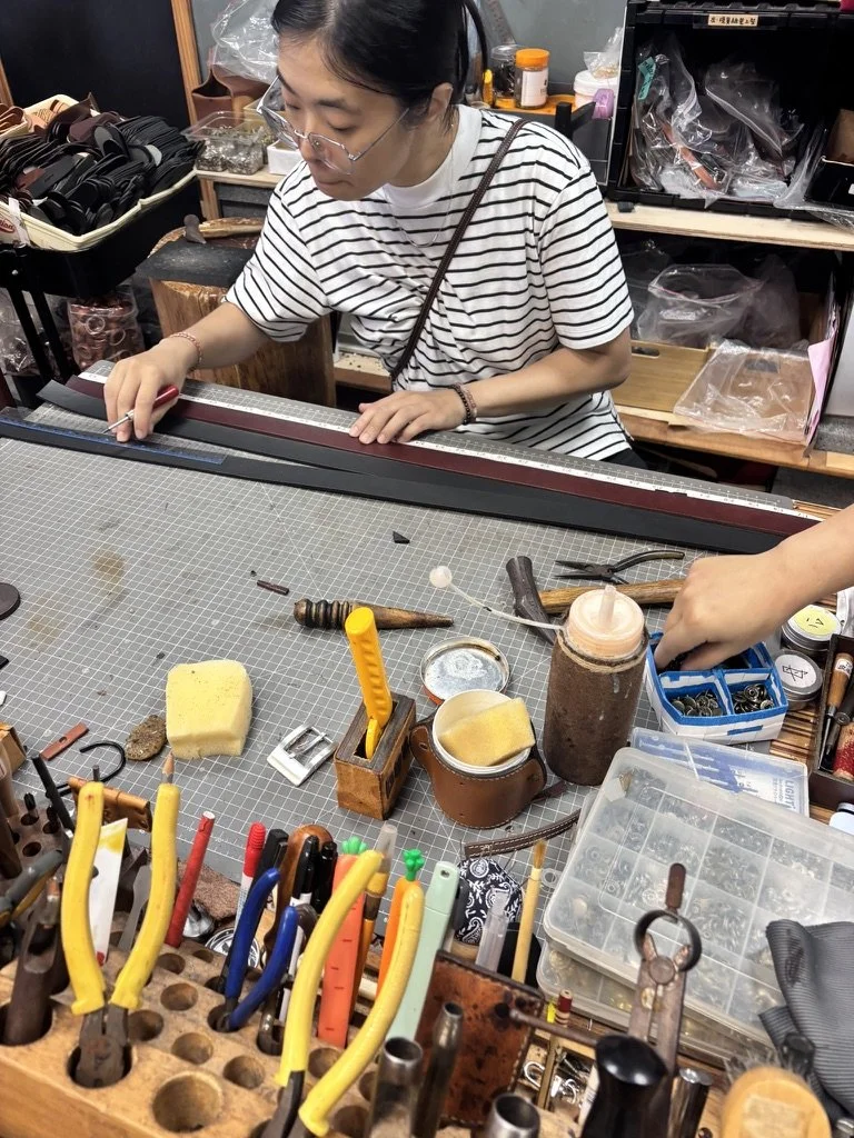 A person working at a craft or jewelry making station with various tools, including pliers, a ruler, and small containers, in a workshop setting.