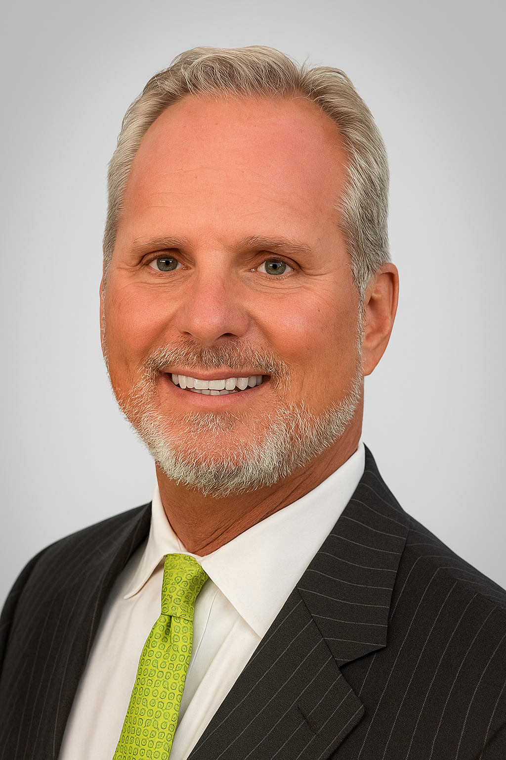 A professional headshot of a middle-aged man with gray hair, beard, and blue eyes, wearing a dark pinstripe suit, white shirt, and lime green tie, smiling against a plain light gray background.