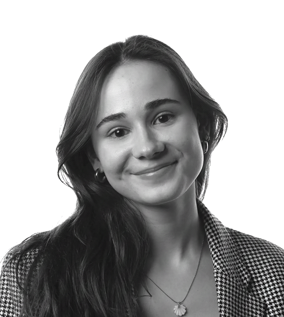 Black-and-white portrait of a smiling young woman (Graphic designer Leonor) with long hair, wearing a plaid shirt and a floral pendant necklace.