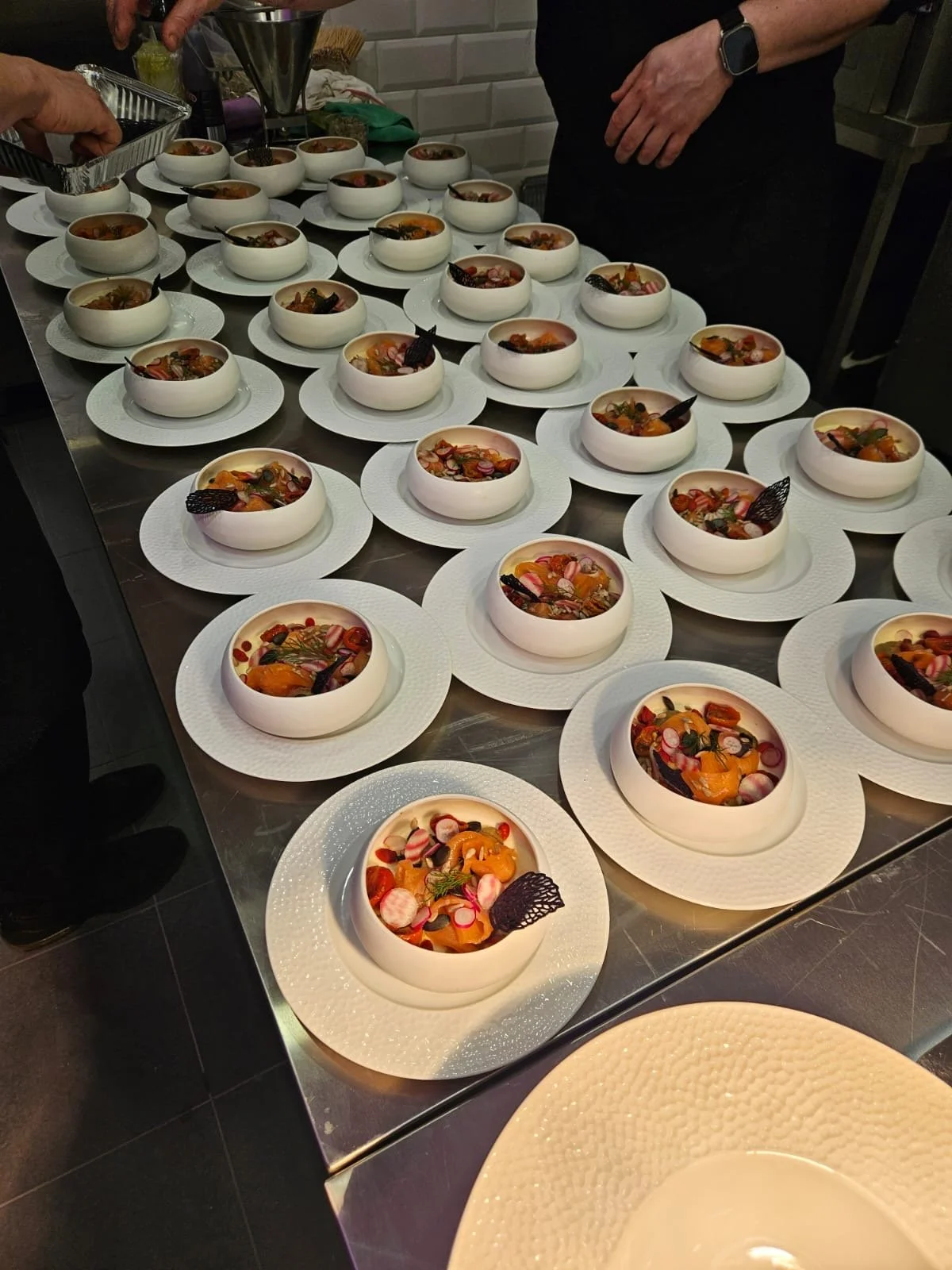 Plats gastronomiques présentés dans des bols blancs, garnis de légumes, fruits, et décorations colorées, sur une table en cuisine