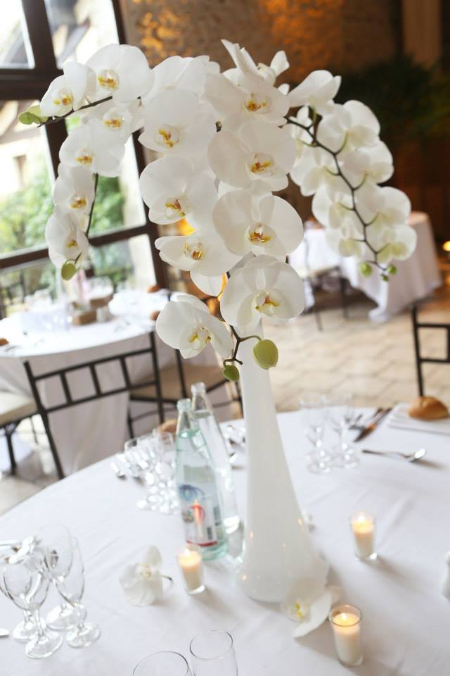 Une grande orchidée blanche dans un vase haut placé sur une table d'événement, décorée de petites bougies.