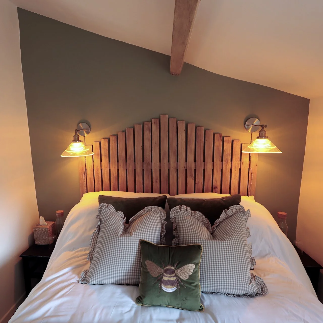 A cozy bedroom with a bed, wooden headboard, pillows, and two wall-mounted lamps.