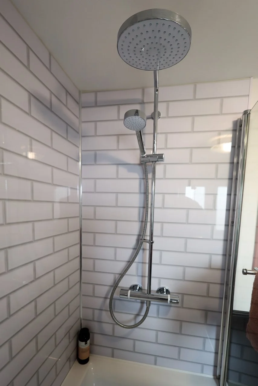 A modern shower with two adjustable shower heads mounted on a chrome bar, set against white brick-patterned tiles.