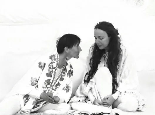 Two women sitting on a bed facing each other, engaged in a conversation.