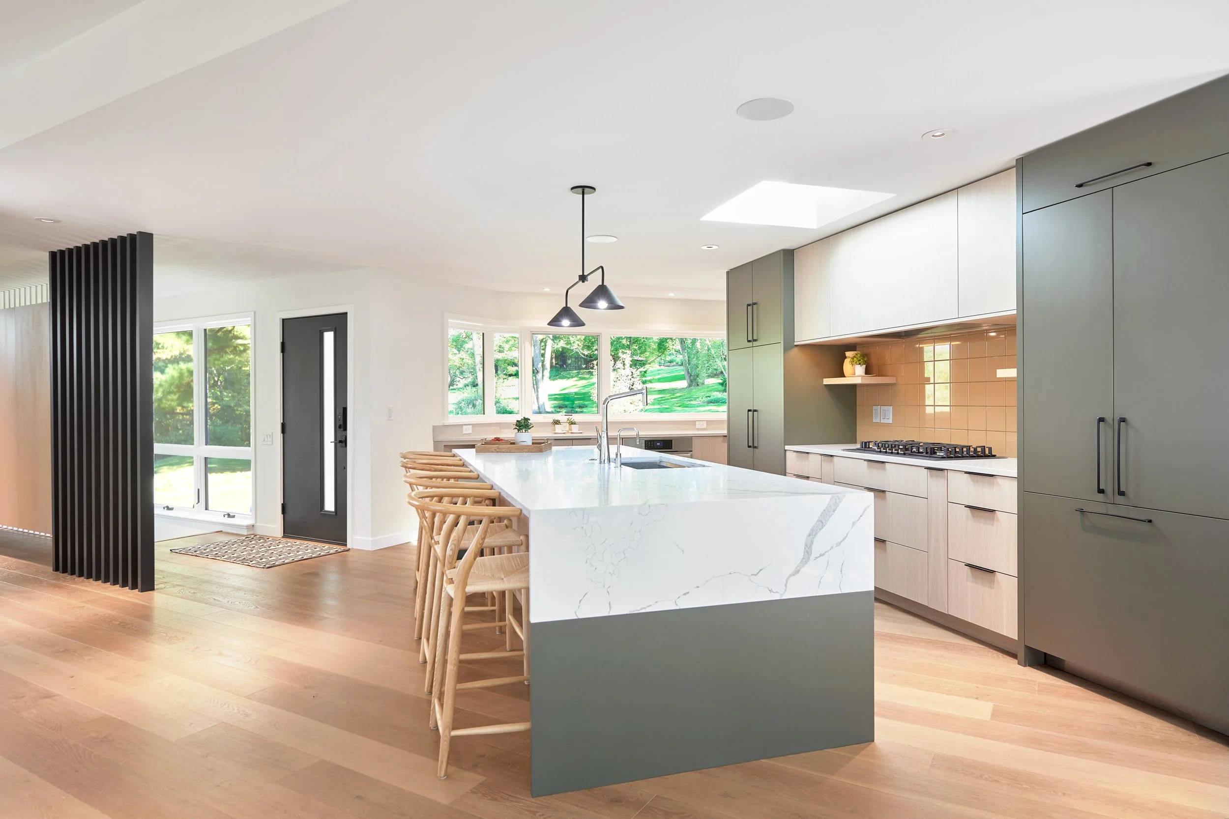 Open concept kitchen in midcentury home. An island topped with white marble sits next to a kitchen range with authentic pink tile backsplash.