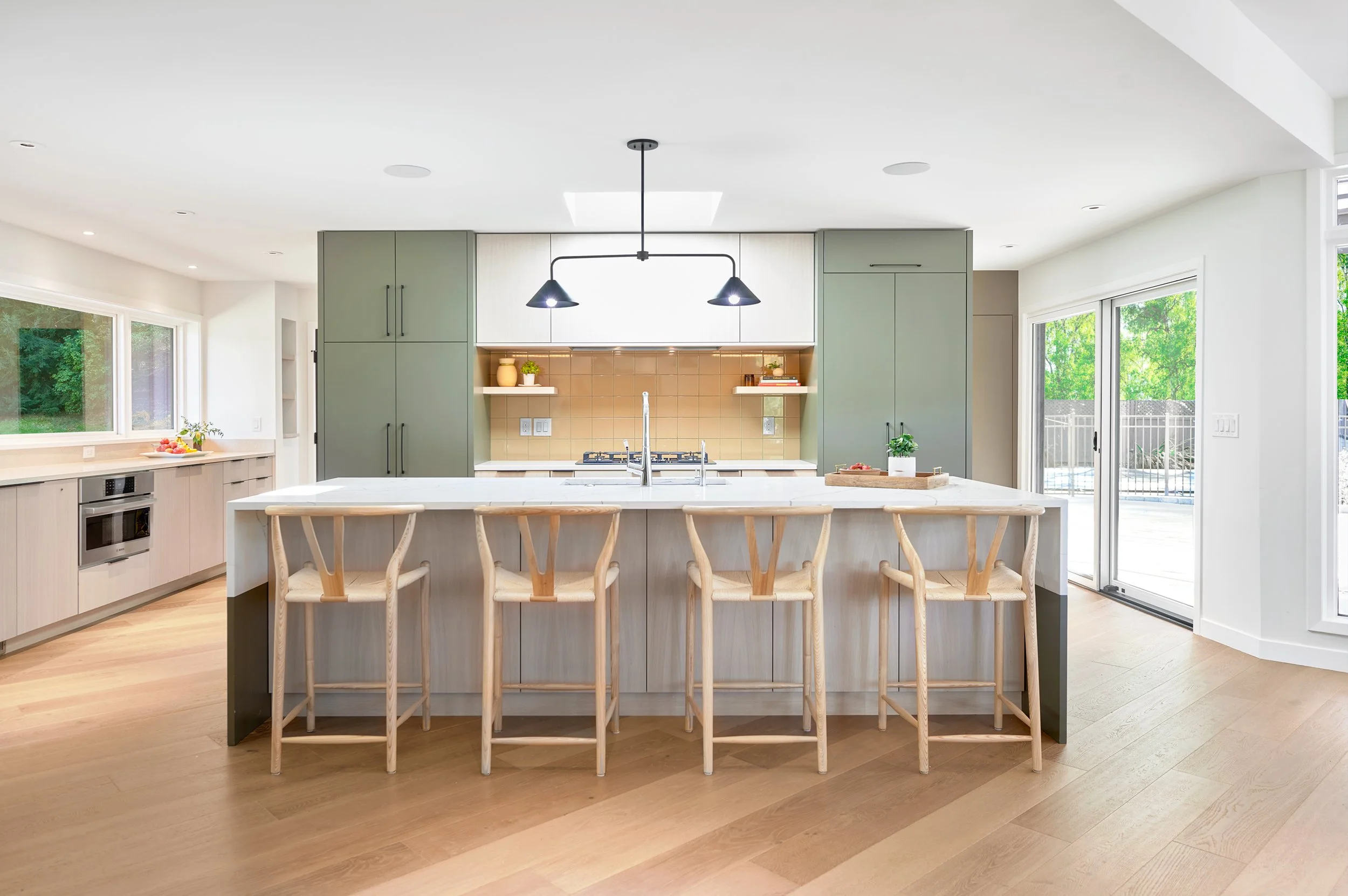 Refreshed midcentury kitchen features a white marble-topped island, updated built-in cabinetry, lots of windows and a glass slider leading to an outdoor patio.