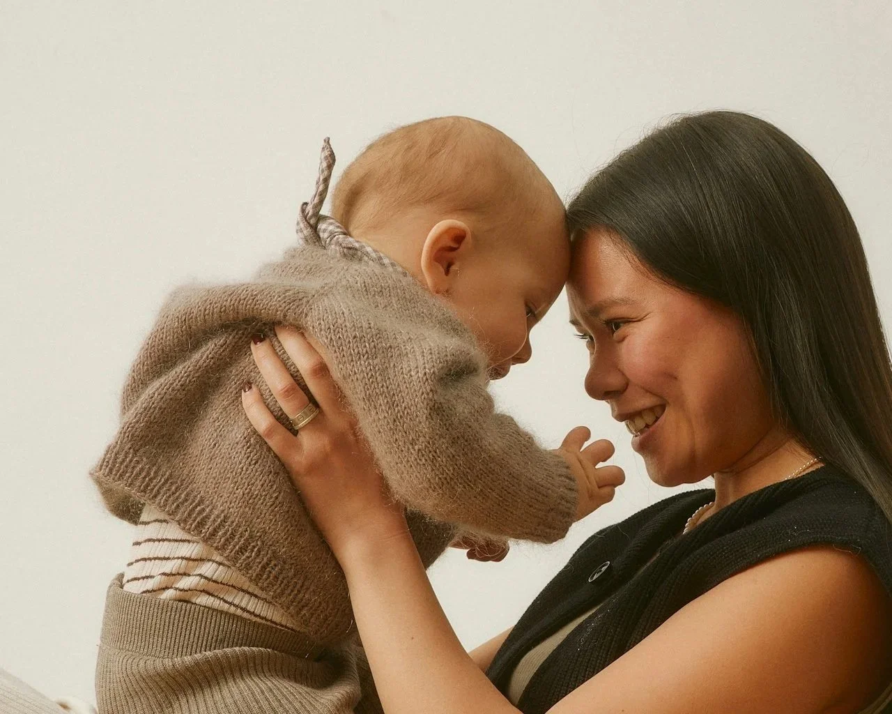 A woman and a young child with their foreheads touching and smiling at each other.