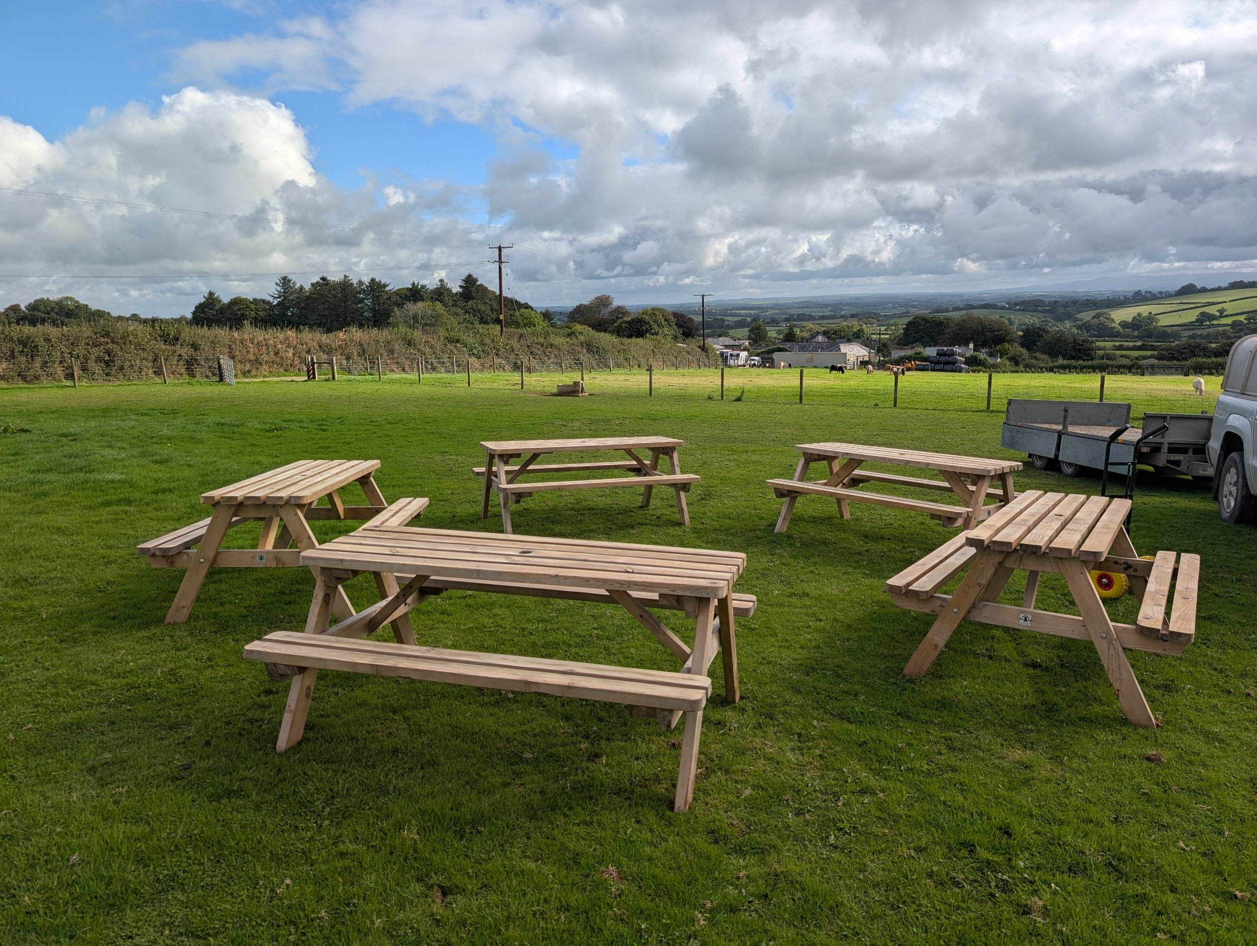 Wooden picnic benches set out on a clifftop green in Cornwall with the sea behind.