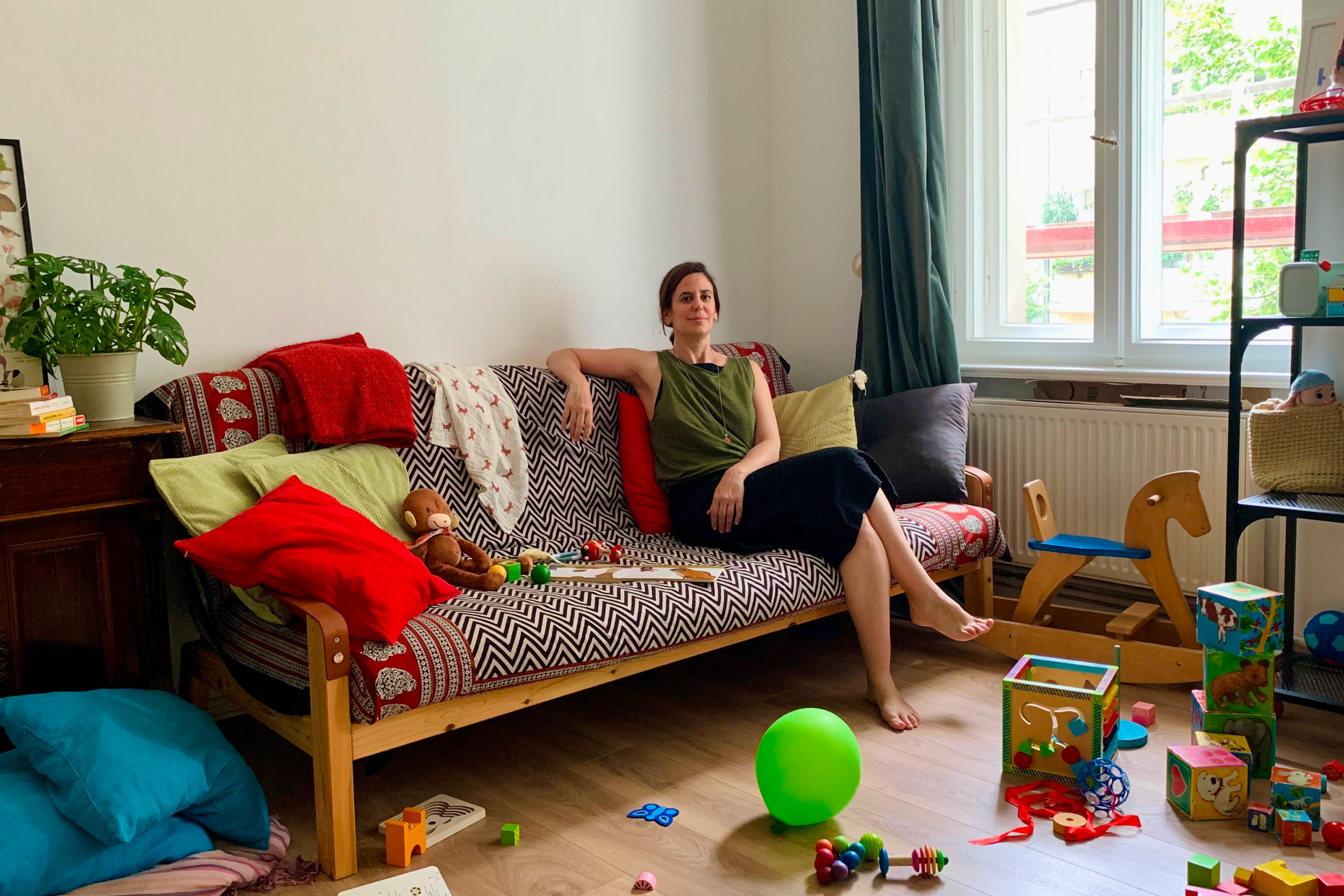 Ana sitting in her studio space with her child's toys on the floor, showing a lively environment