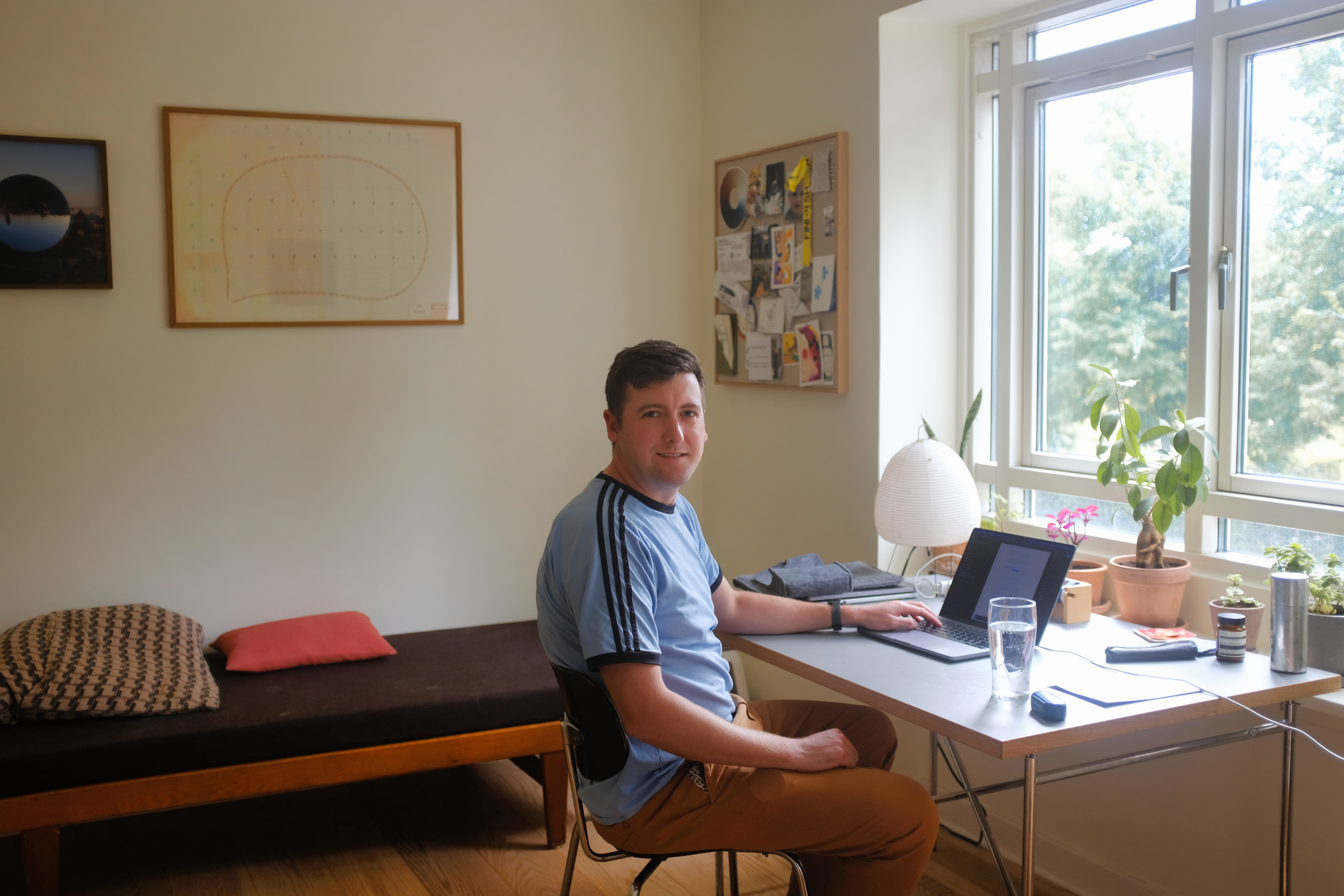 Ciarán sitting at a desk in front of a widow with large trees in the background.