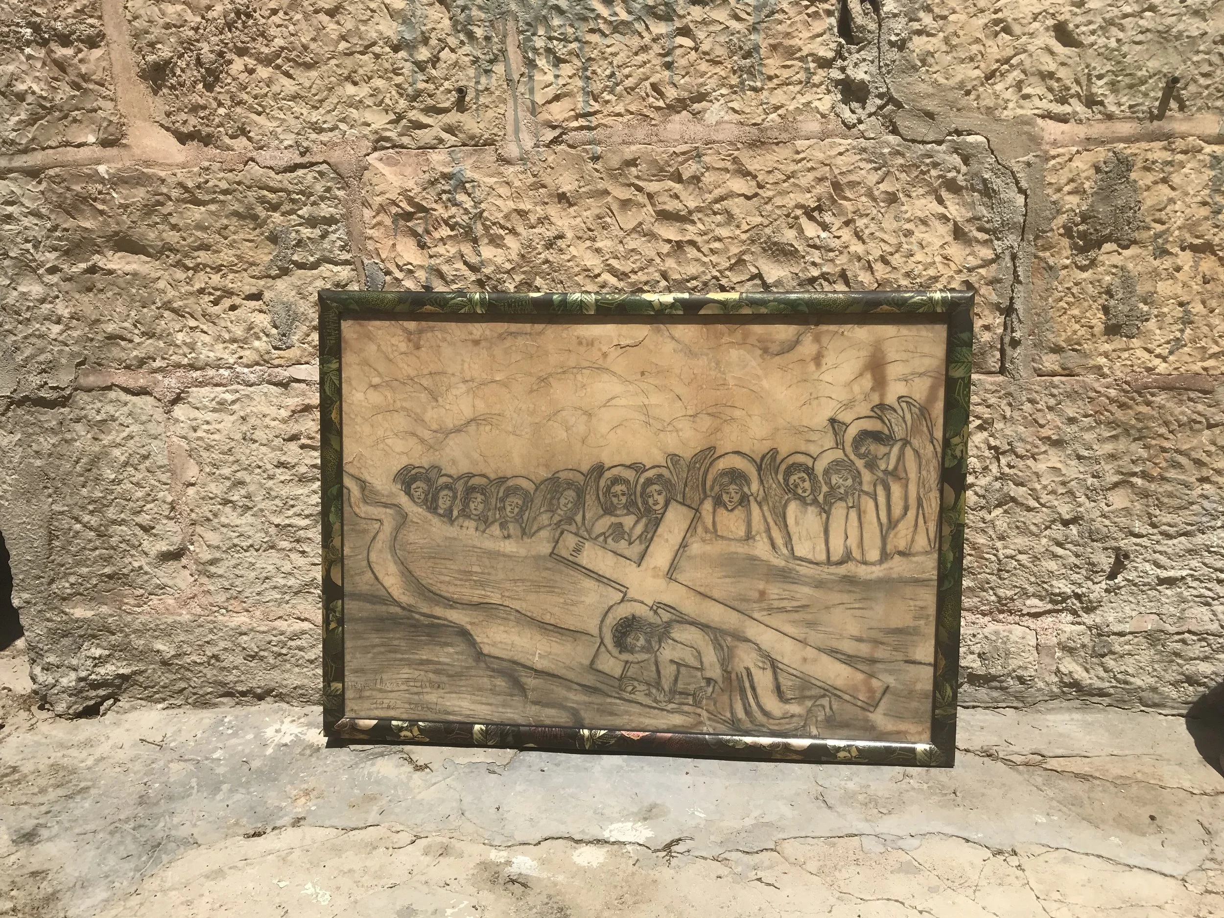 A framed drawing of a group of women sitting together, with some holding books, leaning on a surface, or with their hands on their laps, set against a rustic stone wall background.