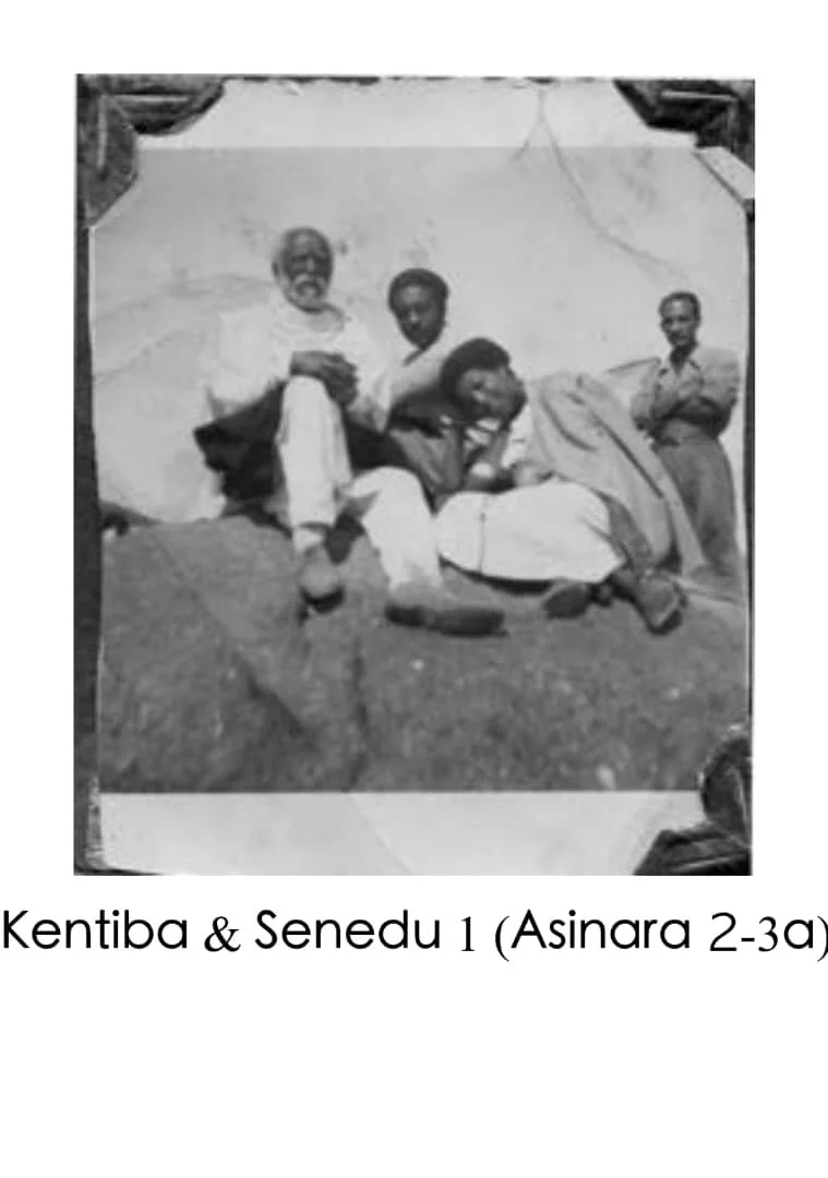 Black and white photo of four men, with two sitting and two standing, in front of a backdrop. The caption reads "Kentiba & Senedu 1 (Asinara 2-3a)."