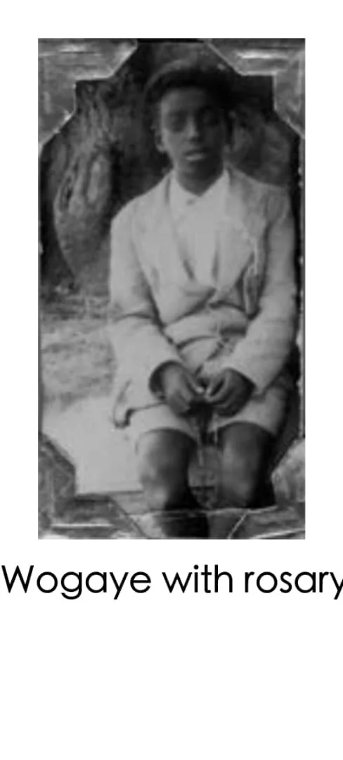 A young boy sitting with his legs crossed, dressed in a white uniform, holding prayer beads, with a rock formation behind him. Text at the bottom reads, "Wogaye with rosary."