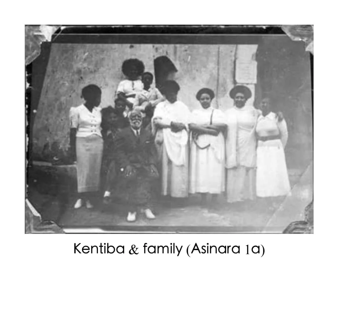 Black and white photo of seven women and three children posing outdoors in front of a wall, dressed in traditional and modern clothing.