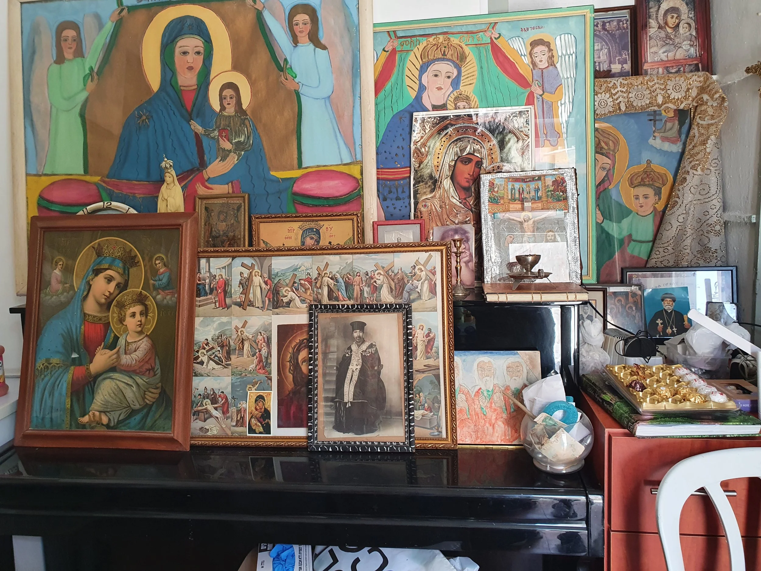 Various religious icons and artwork of Christian saints, particularly representations of the Virgin Mary, arranged on a wall and table with some small religious statues, framed pictures, and religious paraphernalia.