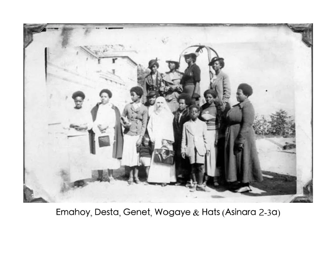 A black-and-white photograph of a group of women and children standing outdoors, some wearing hats, with a building in the background.