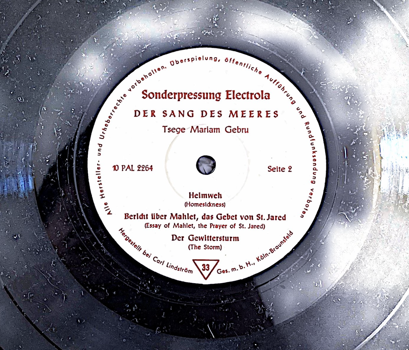 Close-up of a vinyl record with a white label featuring red and black text in German, listing song titles and production details.