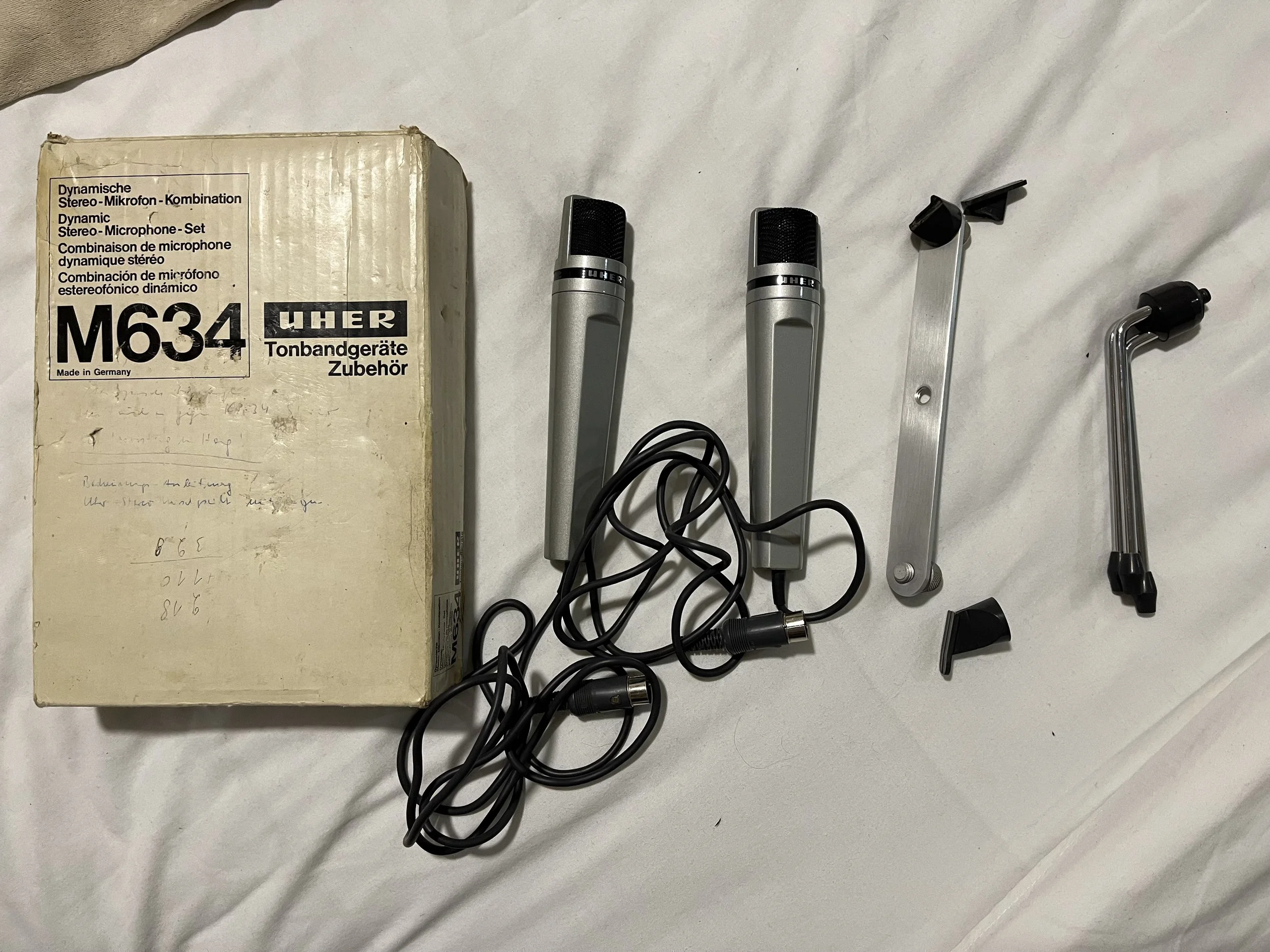 Vintage UHER M634 stereo microphone set with two microphones, metal stands, and a tangled black cable, along with the original packaging box.