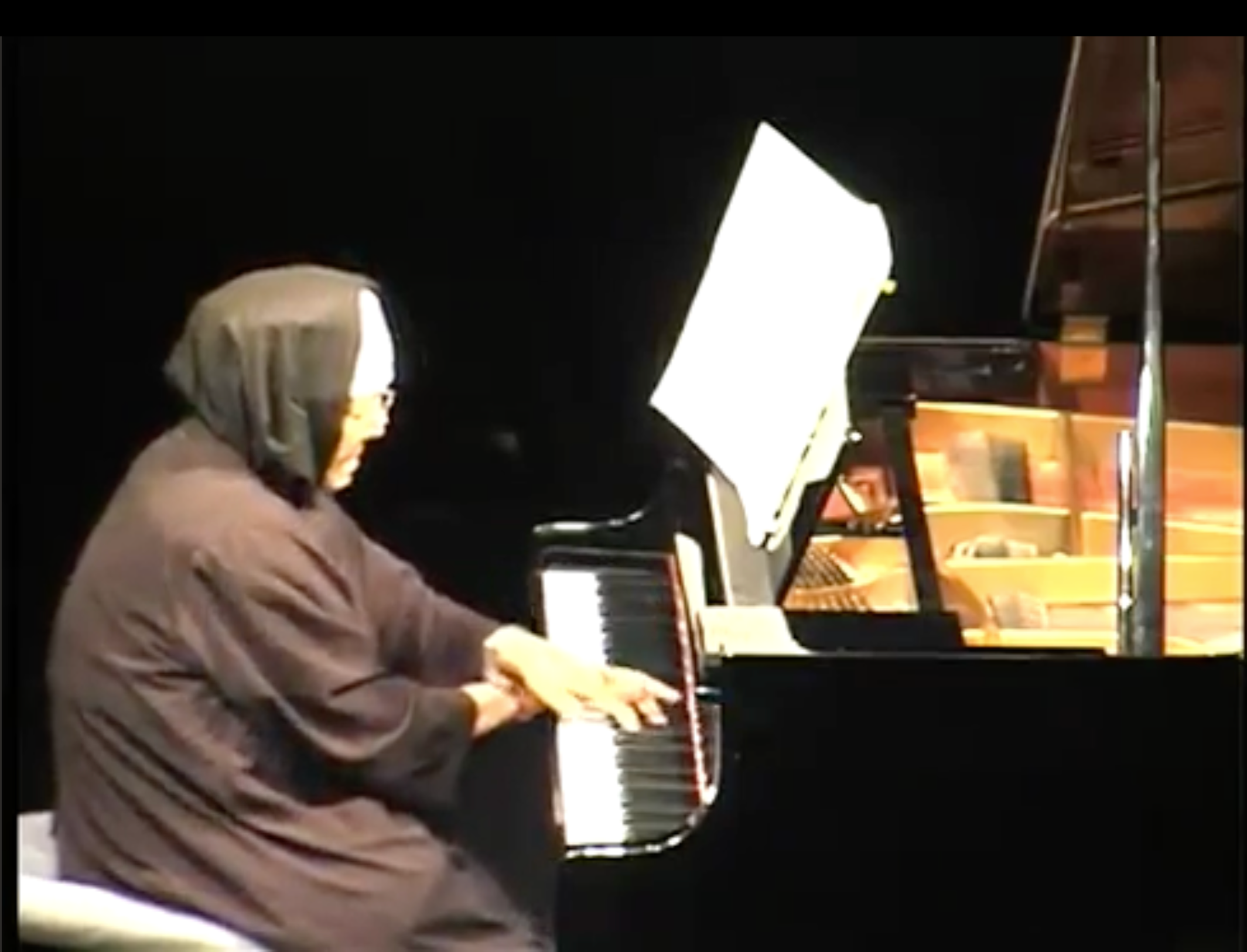 A person wearing a hoodie playing a grand piano.
