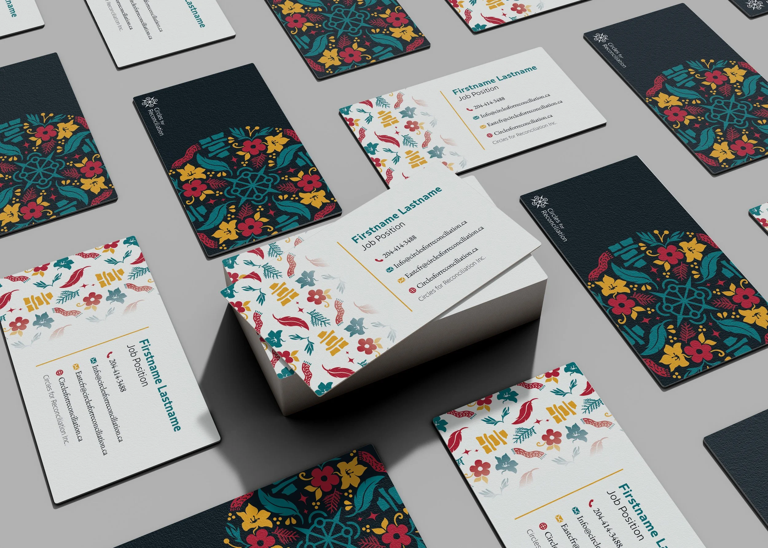 A collection of business cards with colorful floral and geometric designs, arranged on a gray surface, featuring some cards with a dark navy background and others with a white background, displaying contact information and social media icons.