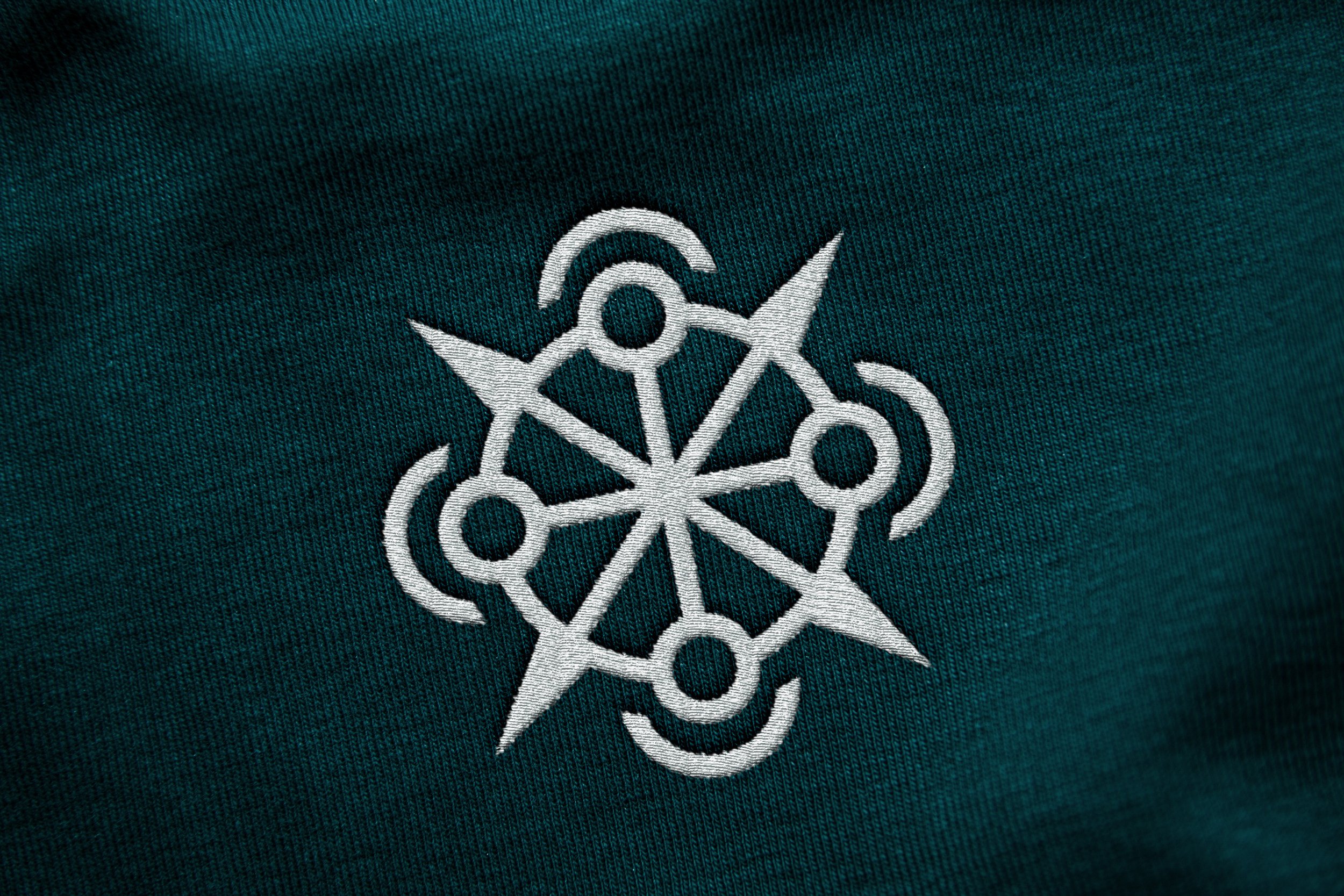 A close-up of an embroidered geometric design in white on a dark green fabric.
