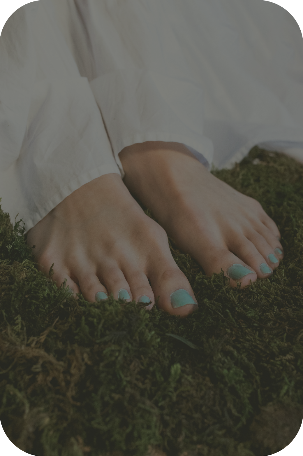 Person's feet with painted toenails resting on green moss, wearing white clothing.