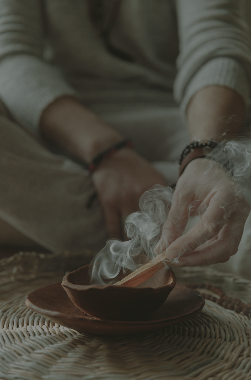 Person holding a matchstick over a bowl of incense, with smoke rising.