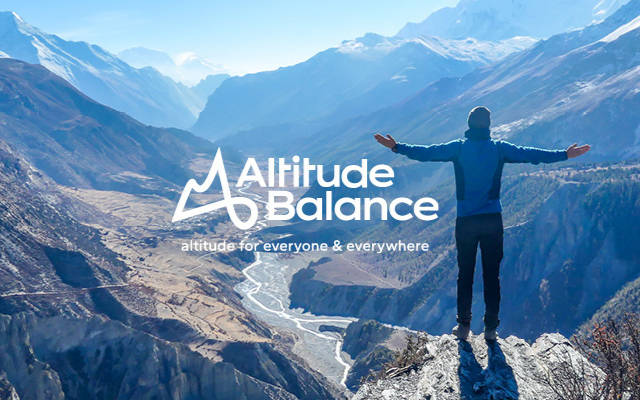 Ein Mann steht auf einem Felsen mit ausgestreckten Armen, blickt auf eine Berglandschaft mit Fluss im Tal und bewölktem Himmel, Logo von Altitude Balance mit Slogan 'Höhe für alle & überall'.