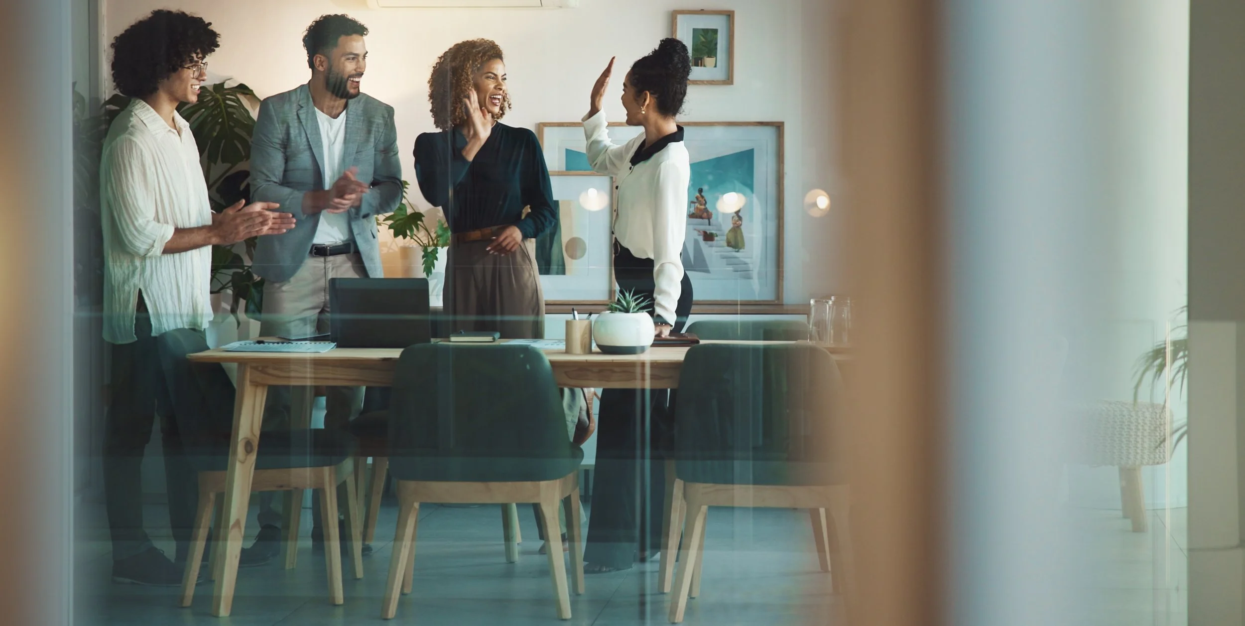 Fünf Menschen in einem modernen Besprechungsraum, die sich freudig begrüßen und miteinander lachen.