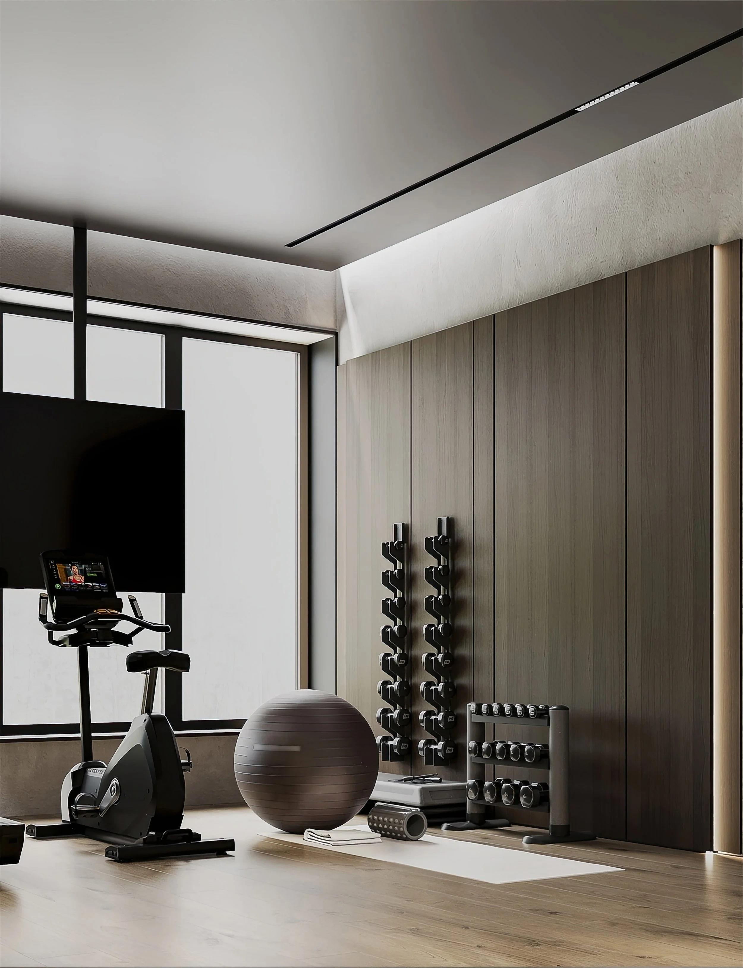 Moderater Trainingsraum mit einem stationären Fahrrad, Gymnastikball, Hanteln, Hantelständer, Yogamatte und verschiedenen Fitnessgeräten, in einem Raum mit Holzboden, großen Fenstern und moderner Einrichtung.