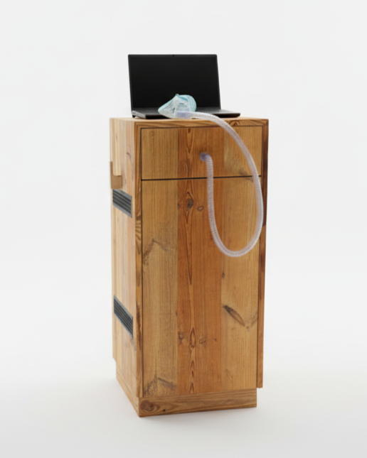 Ein Holzmöbelstück mit einem Laptop auf der Oberseite, verbunden mit einem Schlauch und einer Atemmaske, in einem weißen Raum.