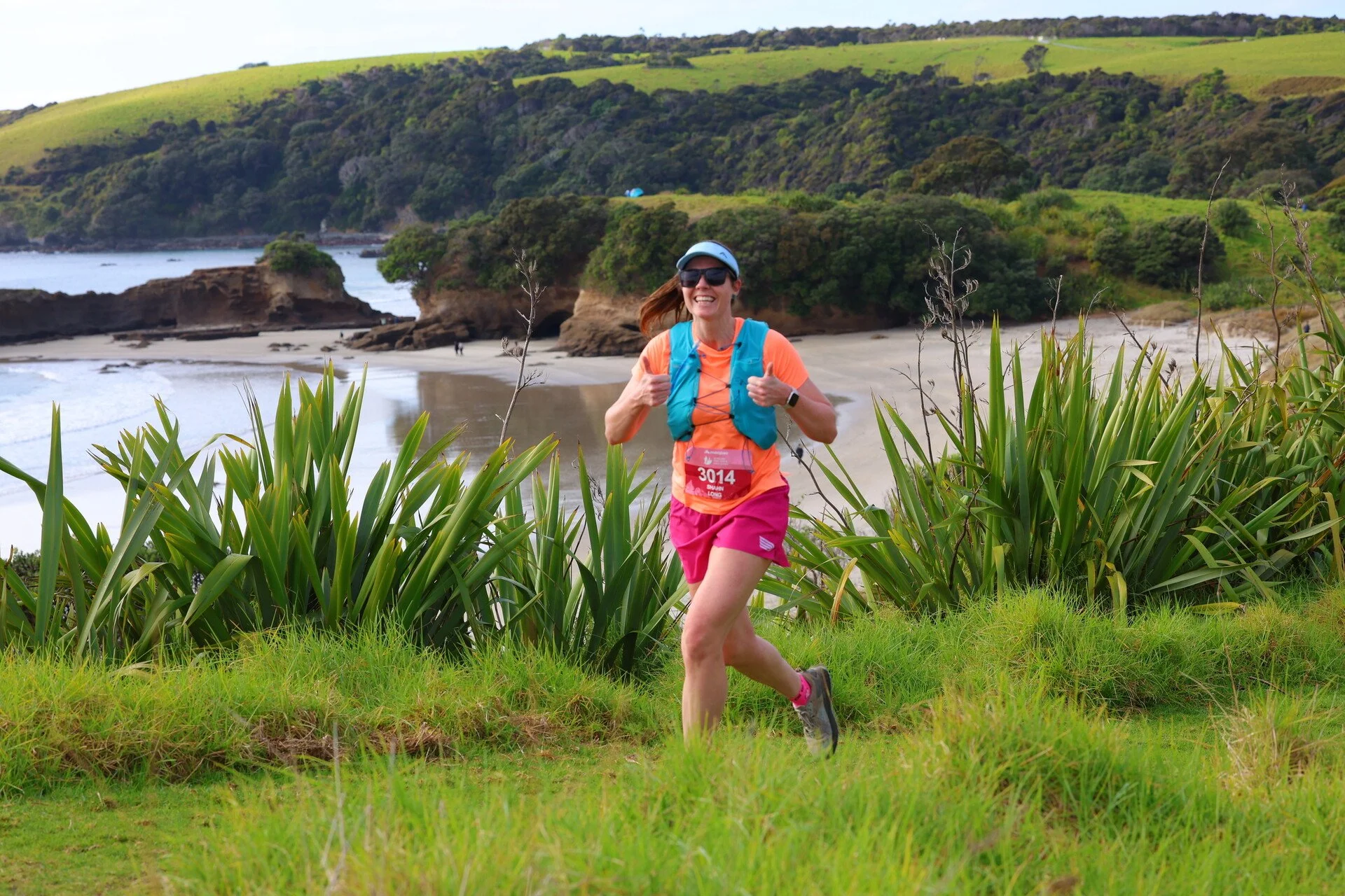 Woman running on a grassy trail with coastal landscape, cliffs, and ocean in the background.