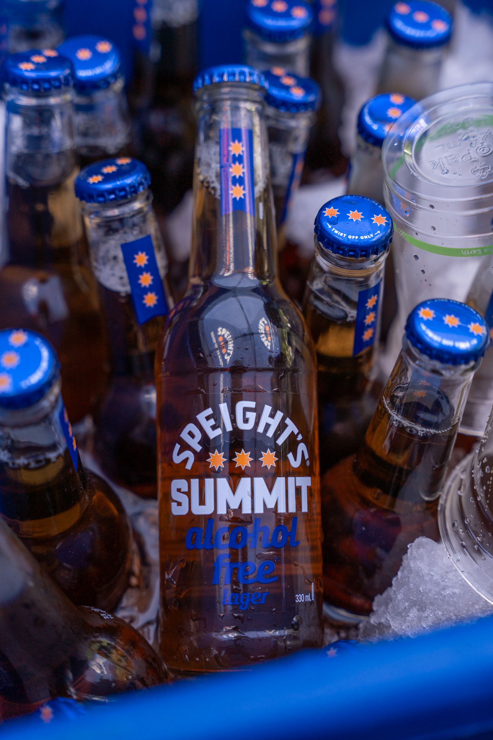A bunch of bottled non-alcoholic beer, labeled as "Speights Summit alcohol free lager," is shown in an ice bucket with frost and condensation, surrounded by ice.