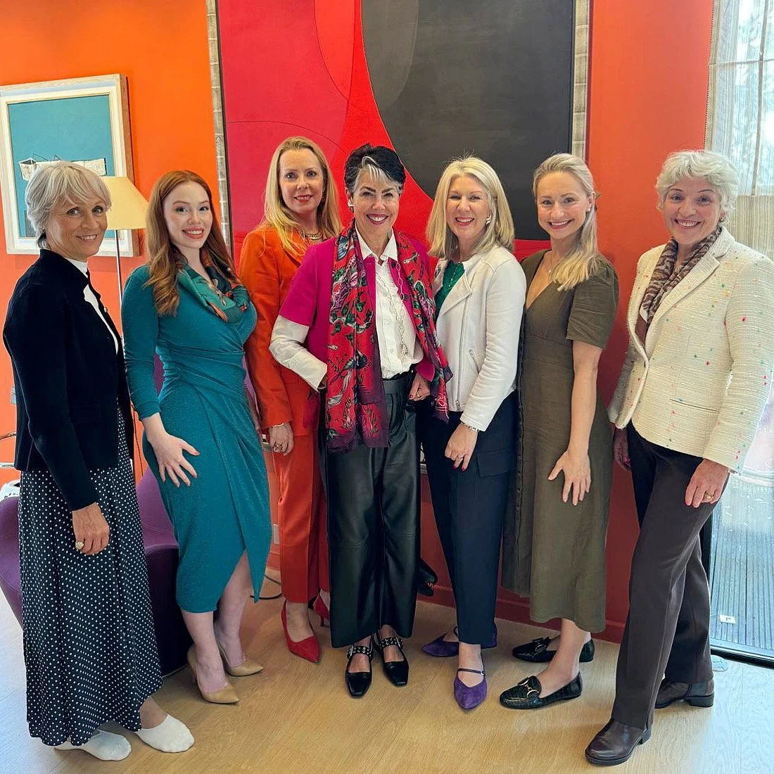 Nine women standing together in a room with colorful walls, smiling for the camera.