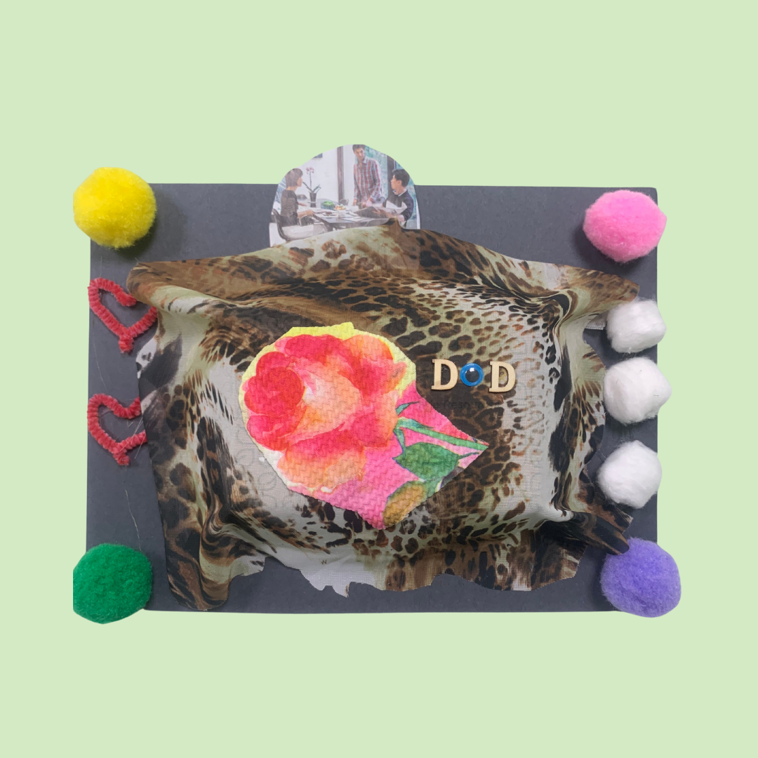 A collage art piece with a black background, a leopard-print fabric base, colorful pom-poms and heart shapes, a floral cutout, a small picture of people dining, and letter beads spelling "DOD".