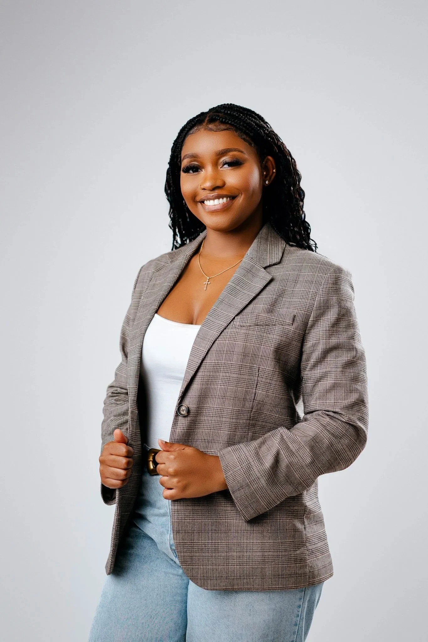 A smiling Black woman in a plaid blazer, white top, and light blue jeans, standing against a plain background.