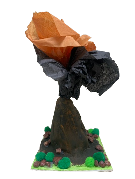 A craft project resembling a volcano made from clay, black and orange tissue paper for the smoke, on a decorated base with green and brown pom-poms.