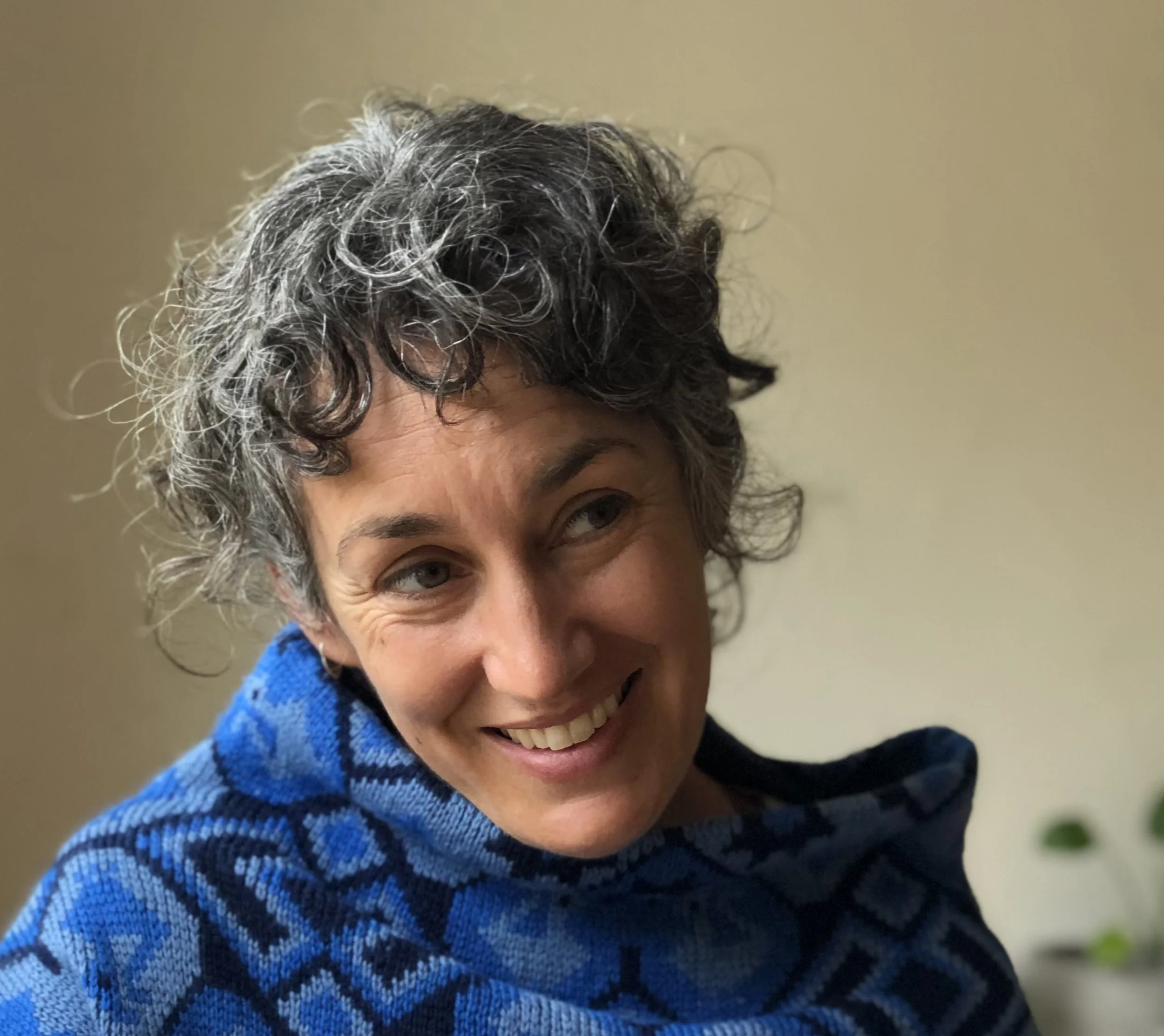 Carly Rose Bretl, LMFT, a woman therapist in Santa Cruz, CA, with curly, short gray hair smiling and looking to the side, wearing a blue patterned sweater.