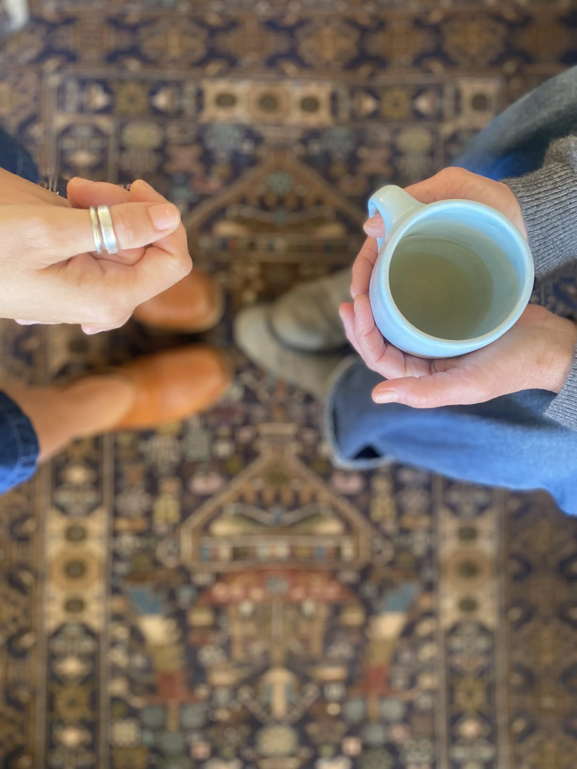 Hands of two people facing each other in the therapy office of Carly Rose Bretl, LMFT, with an ornate rug in the background