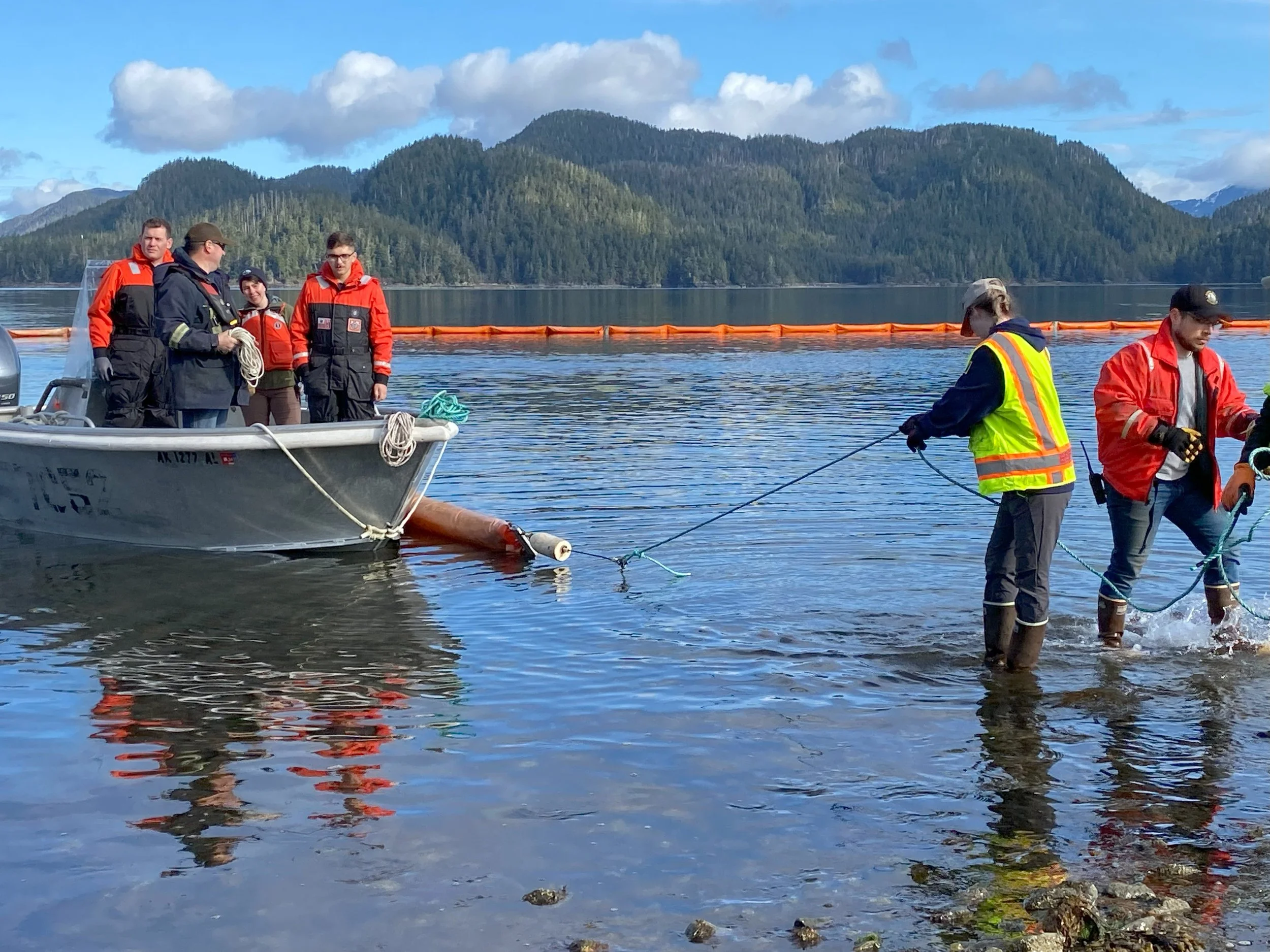 Oil spill response drill with containment boom and response boat on an Alaska waterway with mountains in the background