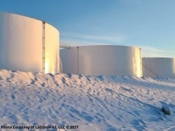 Bulk fuel storage tanks at an Alaska tank farm in winter with snow-covered ground and clear blue sky