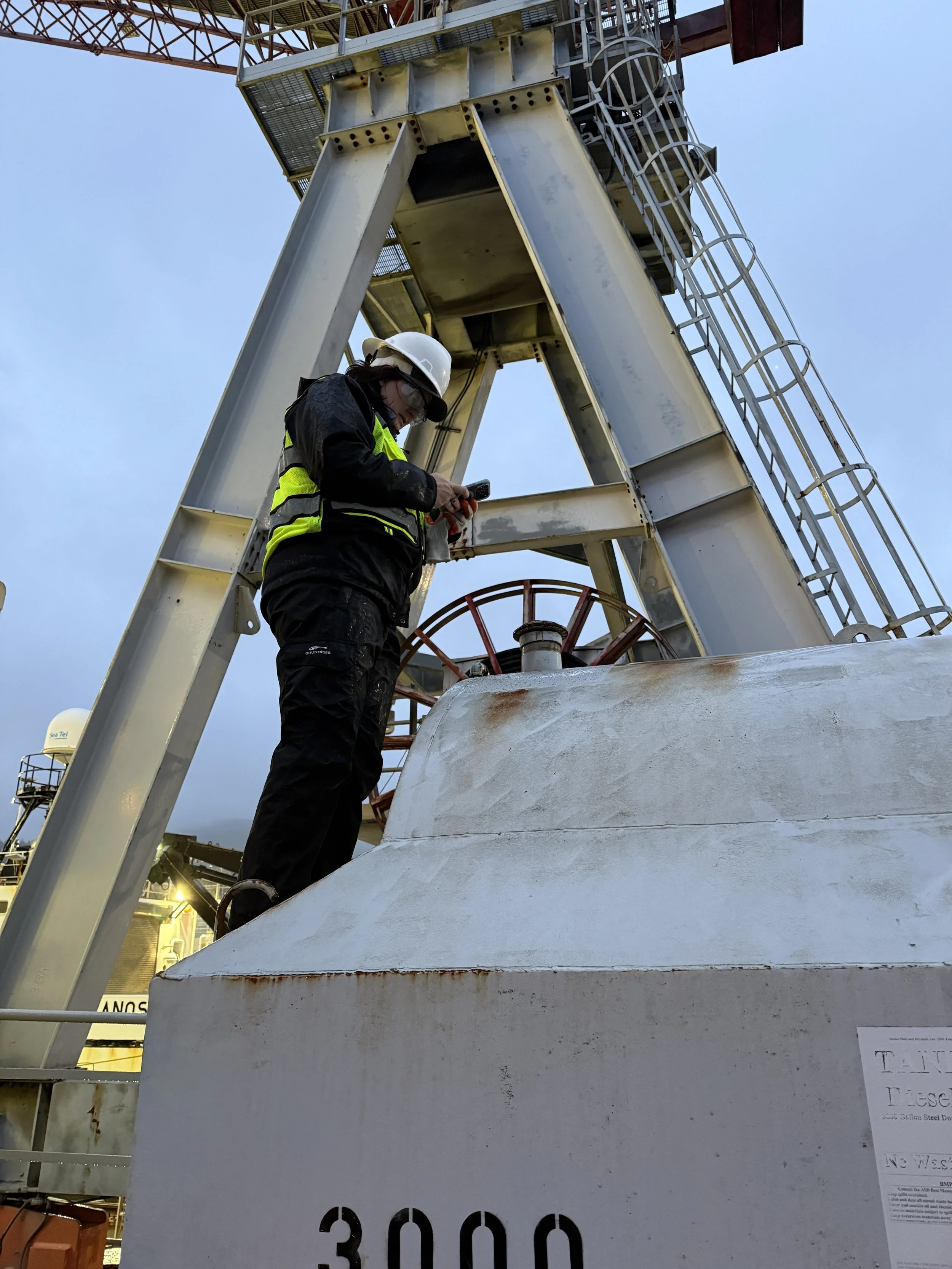 Environmental consultant in safety gear inspecting an aboveground bulk fuel storage tank at an Alaska facility