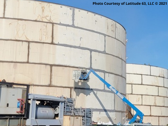 Worker in a boom lift performing maintenance on the exterior of a large bulk fuel storage tank at an Alaska facility