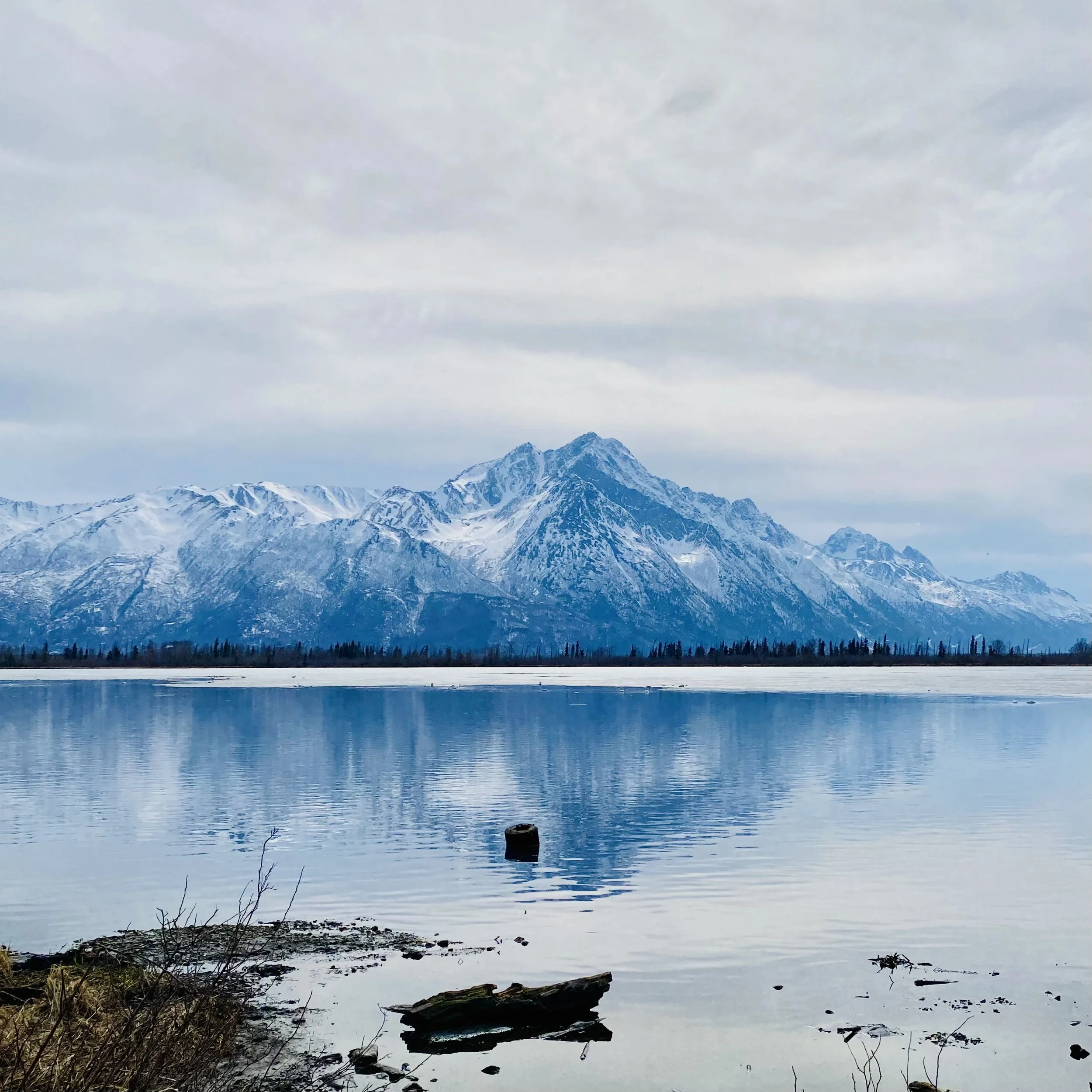 Snow-capped Alaska mountains reflected in a calm lake near an Integrity Environmental project site