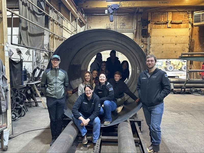 Integrity Environmental team members posing inside a large fuel storage tank section at an industrial fabrication facility