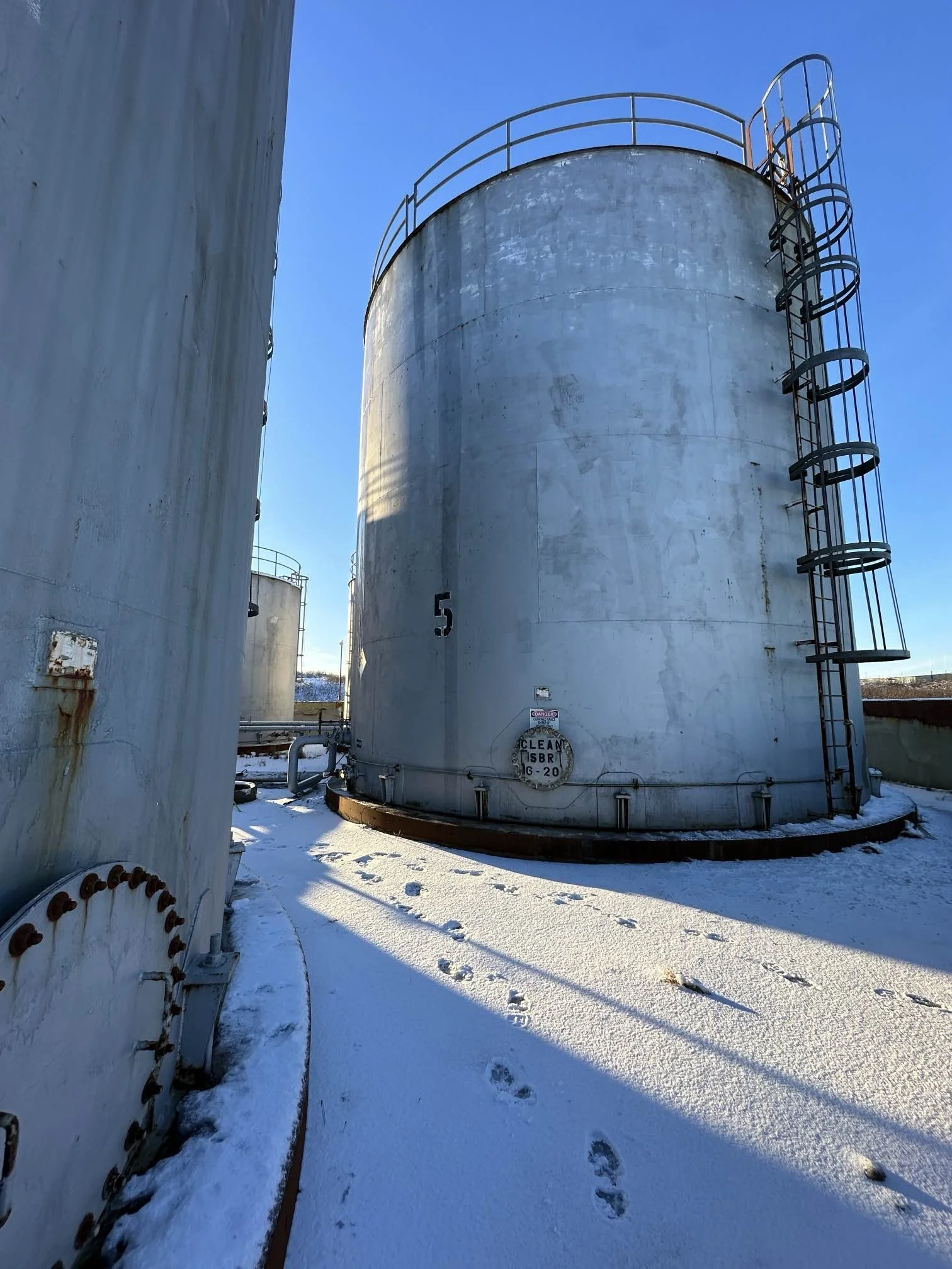Large vertical aboveground fuel storage tank with access ladders and catwalks at an Alaska bulk fuel facility in winter