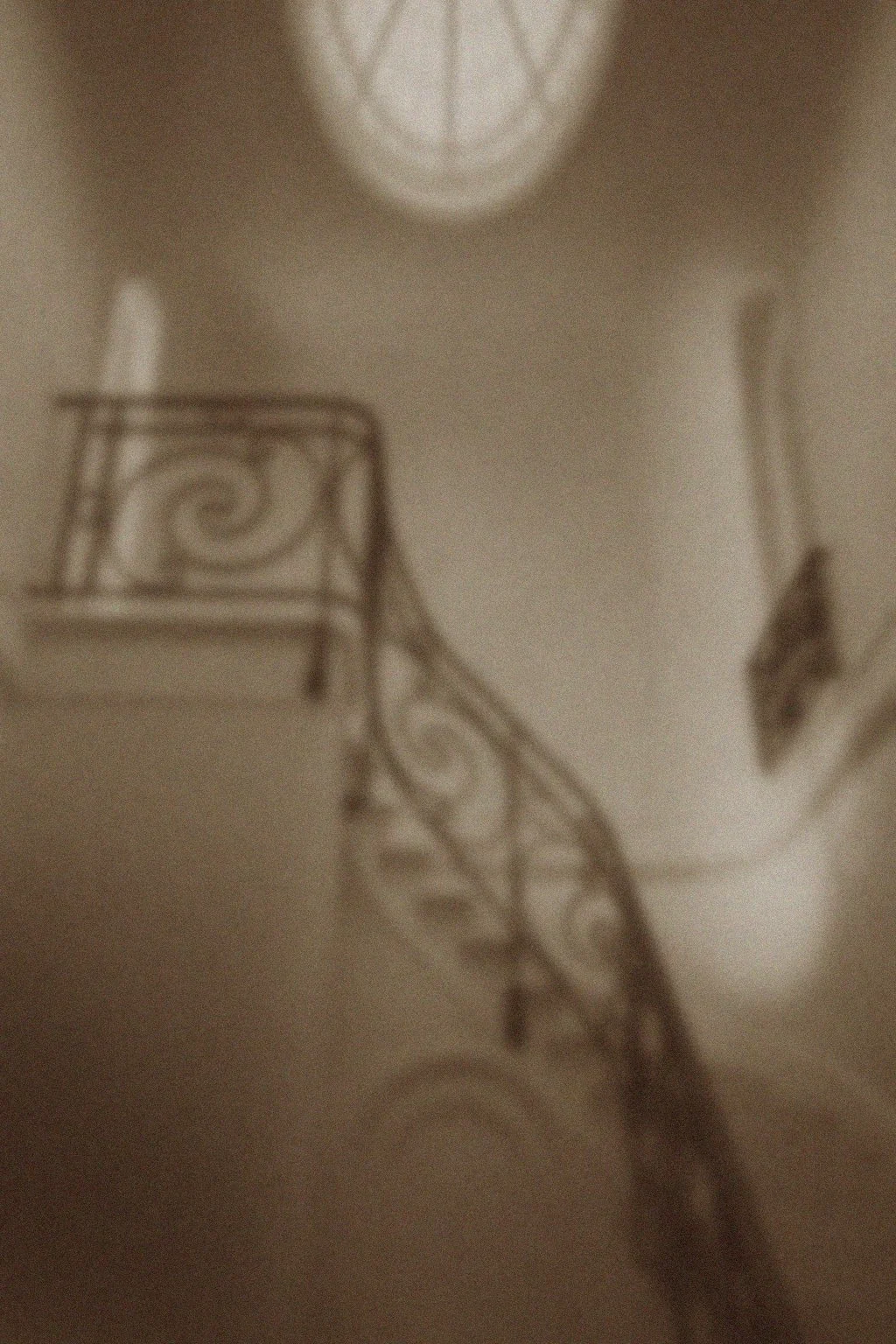 Blurred interior view of a staircase with decorative wrought iron railings, a ceiling light, and framed artwork on the wall.