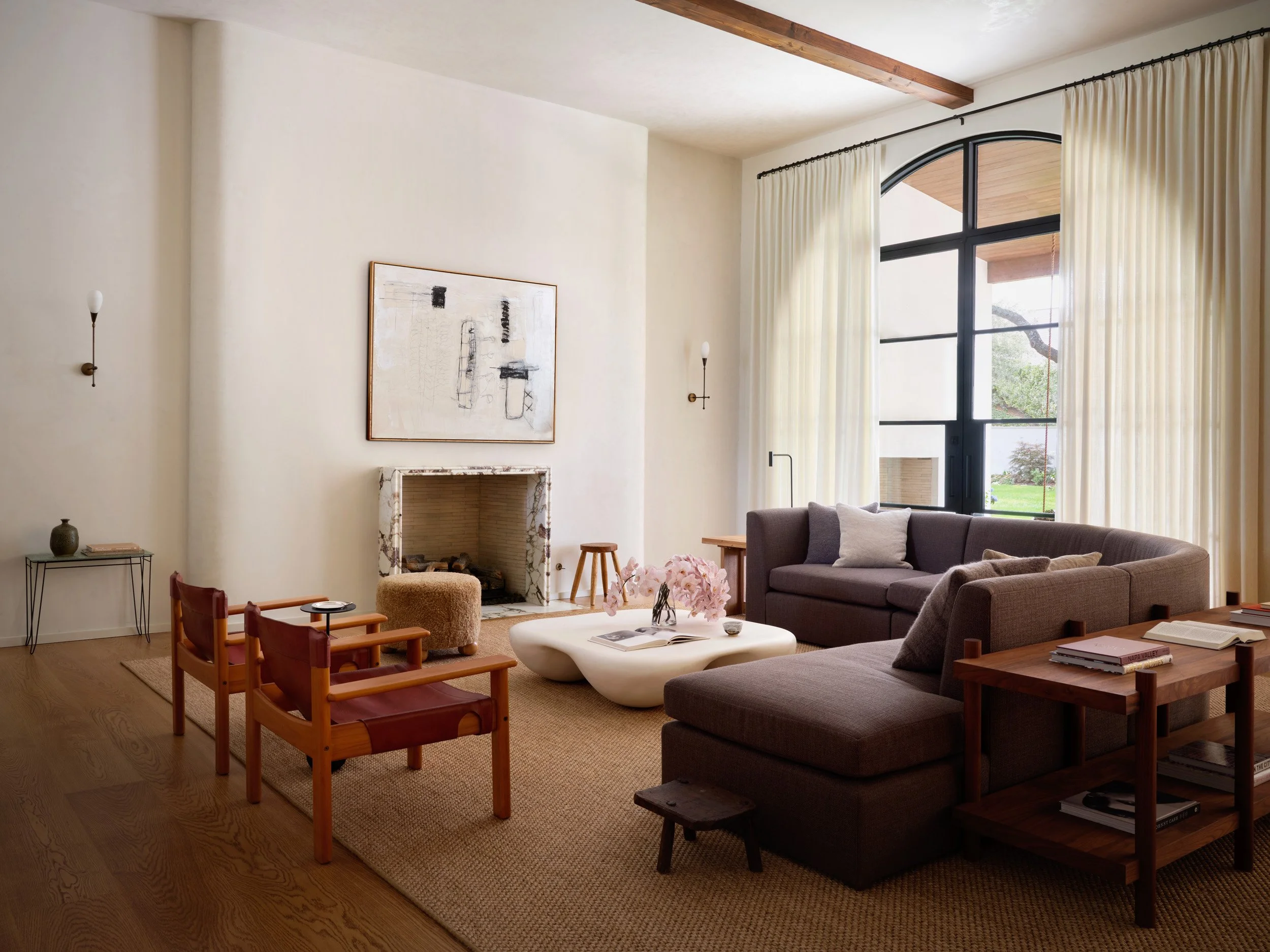 Living room with modern furniture, large window, cream curtains, fireplace, and artwork on the wall.